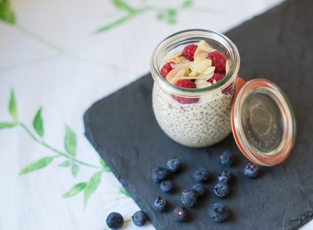 Glas auf Schiefertafel, gefüllt mit Chiapudding, Himbeeren und Mandelplättchen