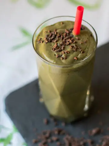 Glas mit grünem Smoothie und rotem Strohhalm, garniert mit Kakaonibs