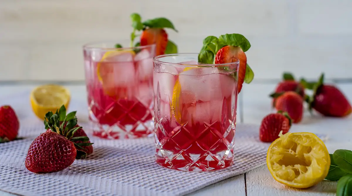Zwei Gläser gefüllt mit Wasser, Erdbeeren, Zitronenscheiben, Eiswürfeln und Basilikum.