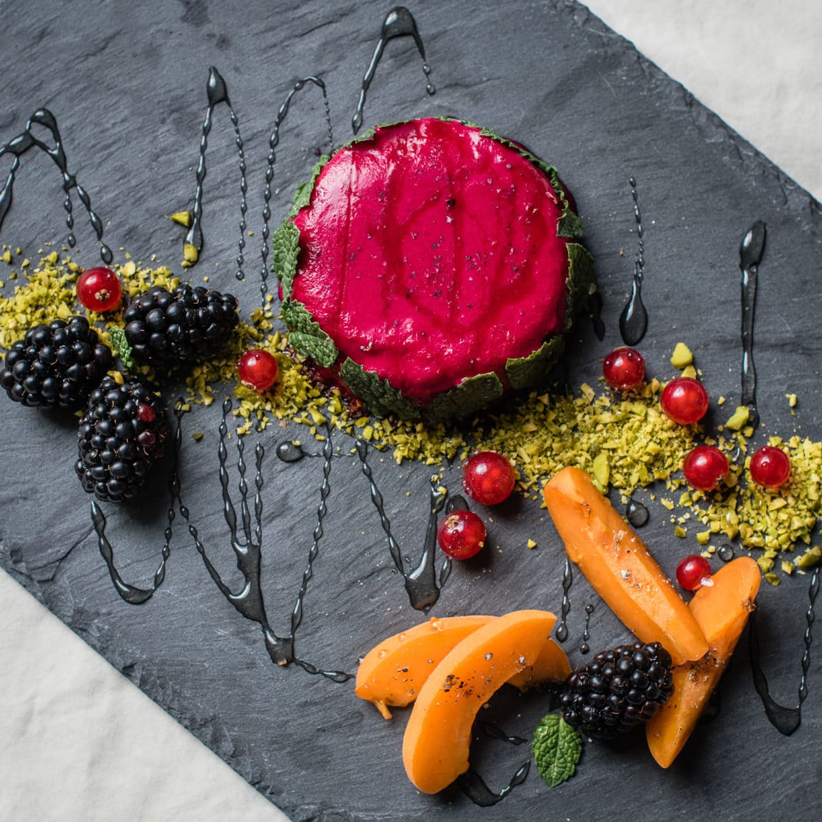 Pinne das Foto, um das Rezept für das pinke Kokos Panna Cotta zu speichern! Topshot von Pinkem Panna Cotta mit frischen Früchten auf Schieferplatte angerichtet