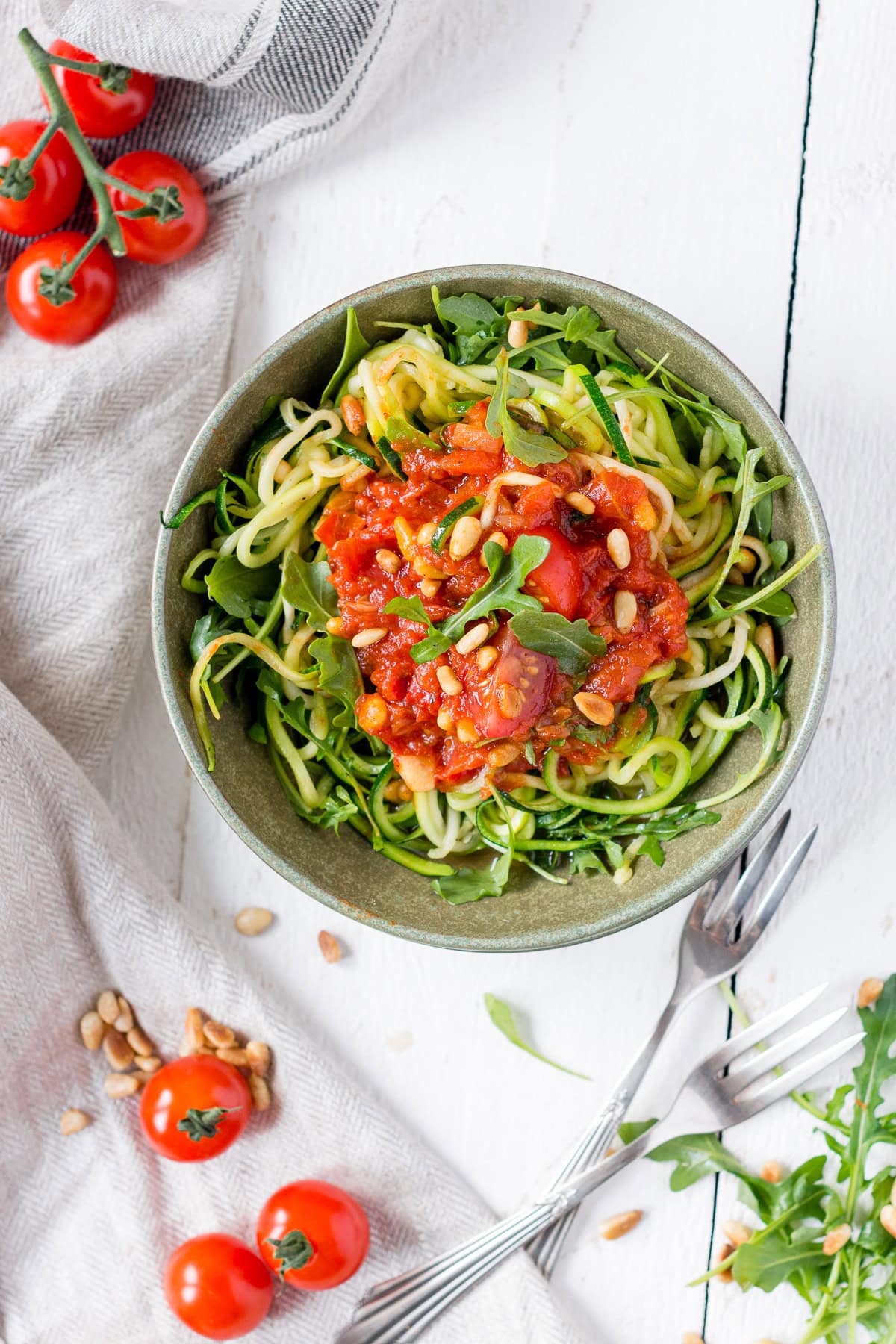 Topshot von Teller mit Zucchini Pasta: Nudeln mit Rucola, getoppt mit Tomaten und Pinienkernen