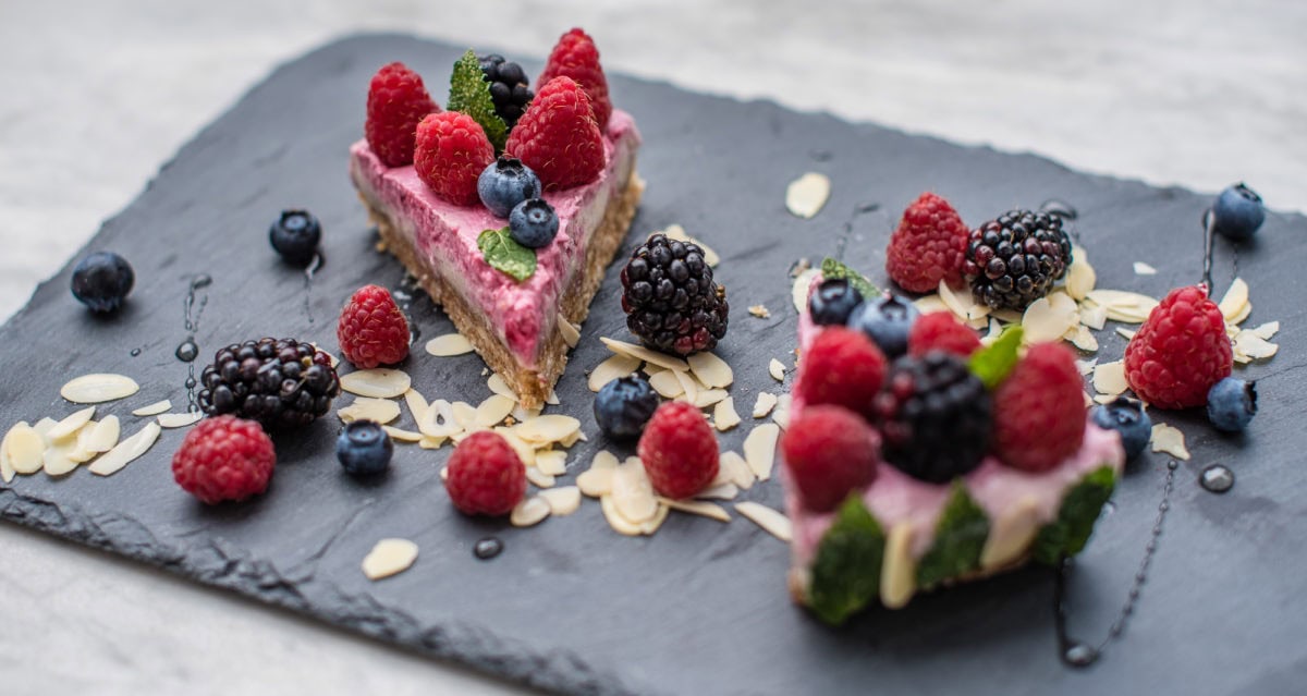 Seitliche Ansicht von zwei Kuchenstücken auf Schieferplatte, garniert mit bunten Früchten