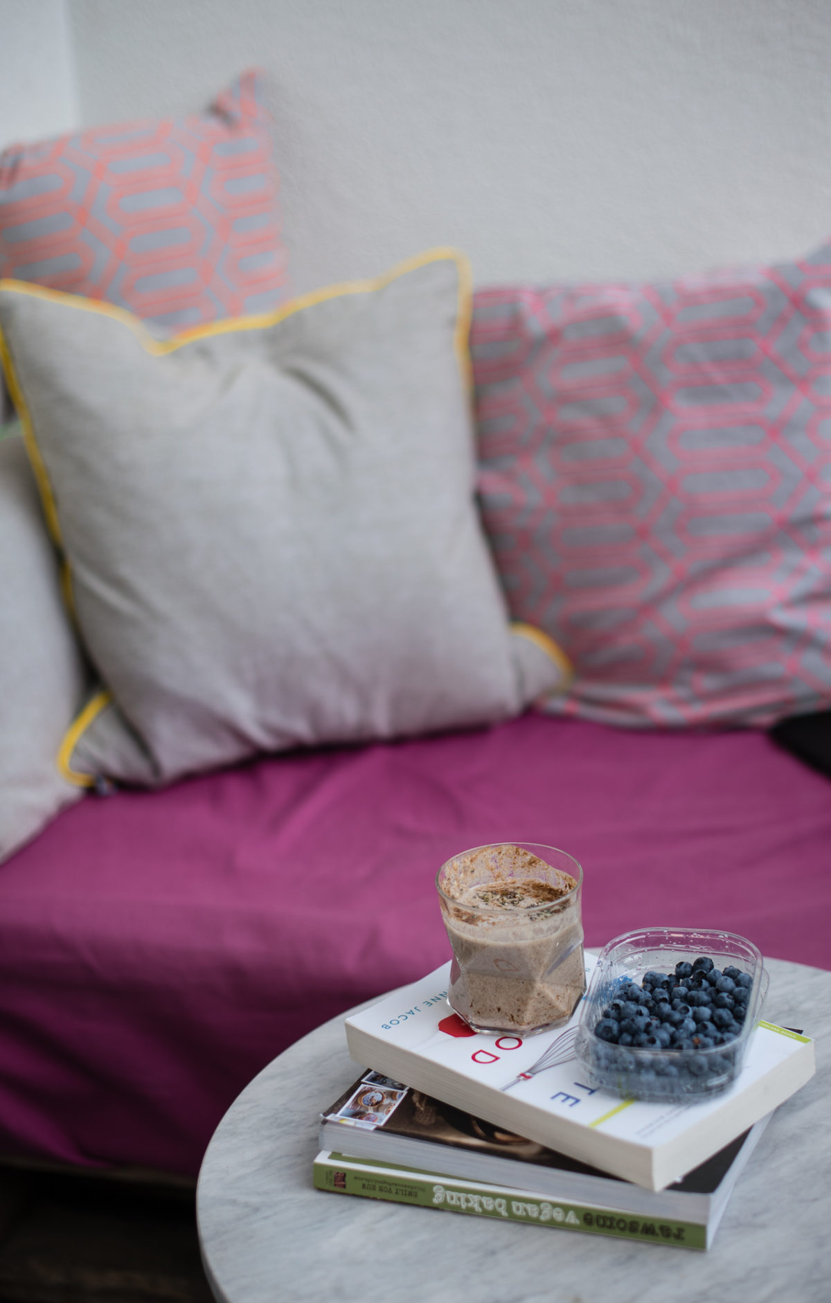 Sitzecke mit Iced Chai Latte im Glas auf kleinem Tisch, dazu Bücher und Blaubeeren in Plastikschale