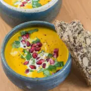 Dunkelblaue Schüssel mit gelber Suppe, garniert mit Granatapfelkernen und Körnerbrot