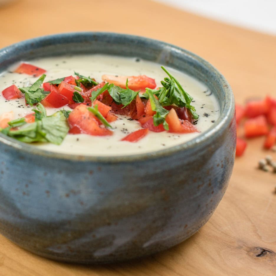 Helle Cremesuppe in Schüssel, garniert mit Paprika und Petersilie.