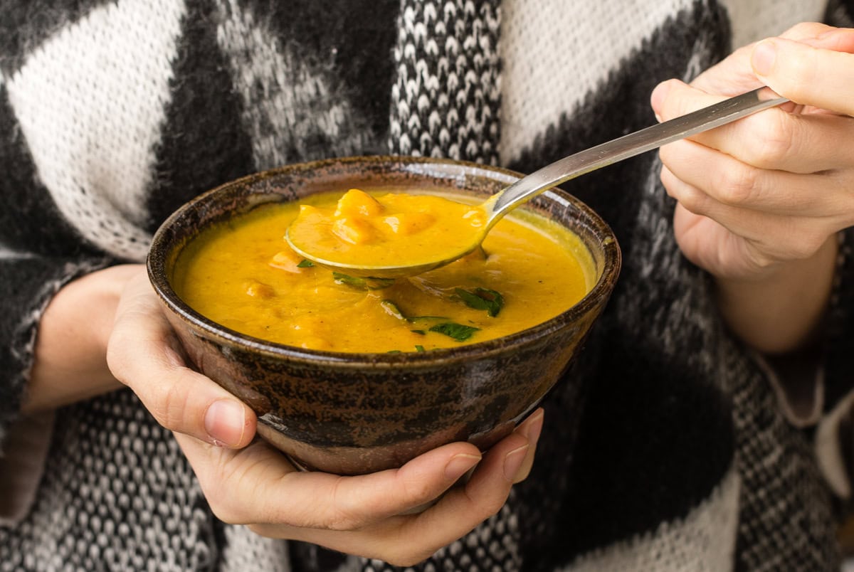 Hände halten braune Schüssel mit gelber Suppe