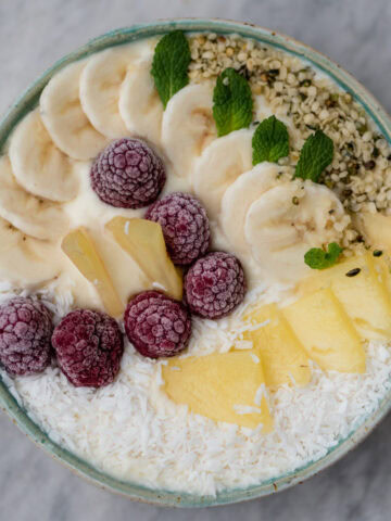 Topshot von Smoothiebowl getoppt mit Himbeeren, Banane, Ananas und Kokosflocken