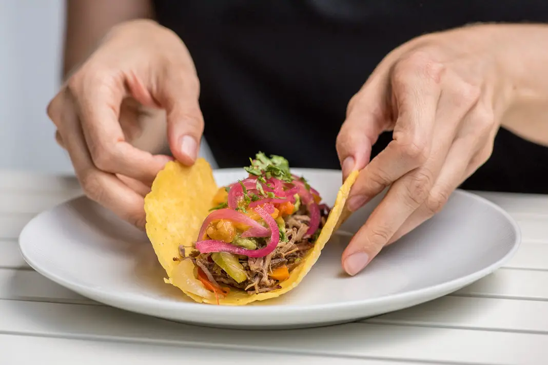 Hand rollt befüllten Taco auf weißem Teller