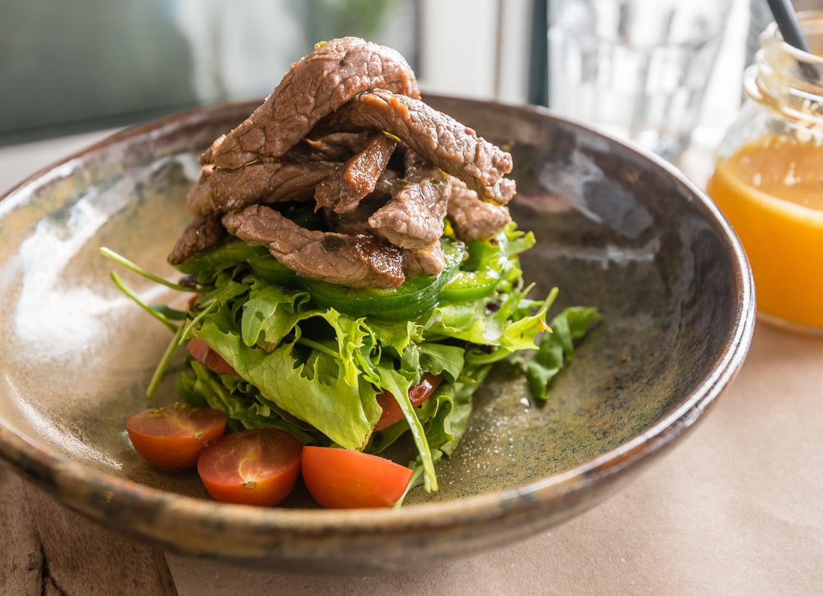 Teller mit hoch geschichtetem Salat und Fleischtopping