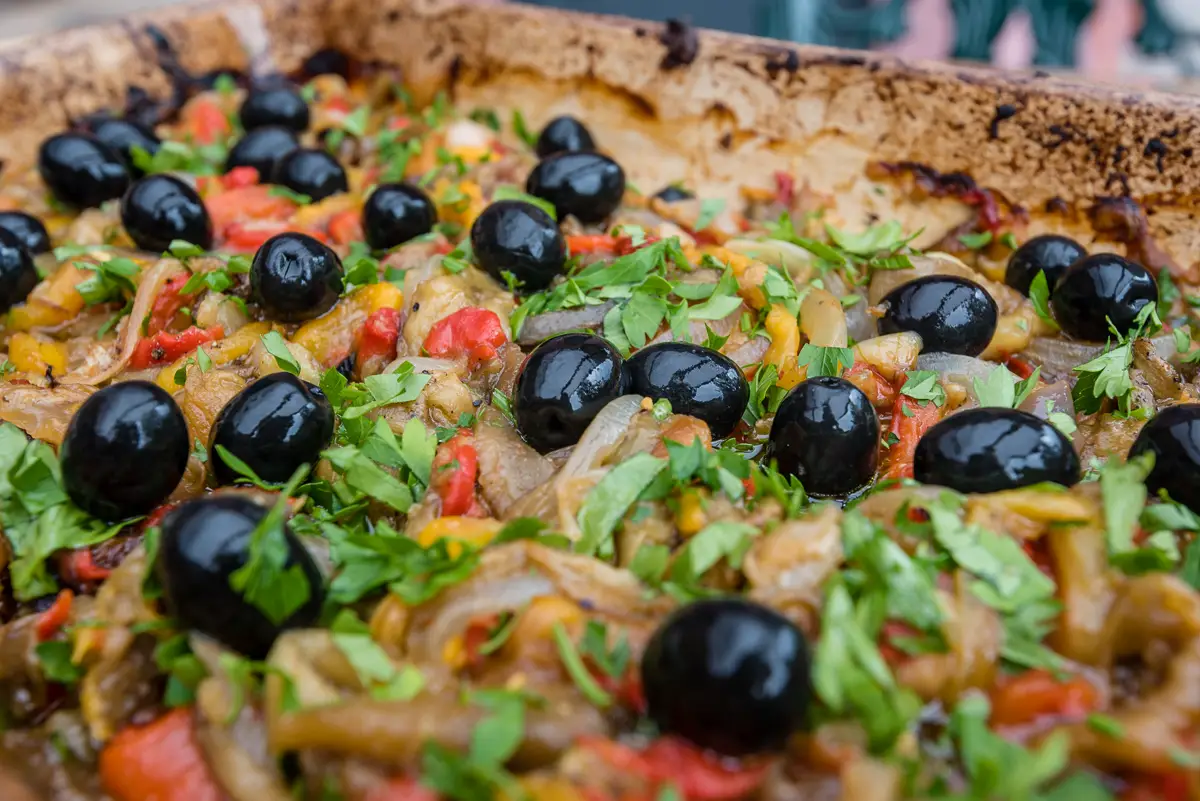 Nahaufnahme von Pizza mit dunklen Oliven und Petersilie