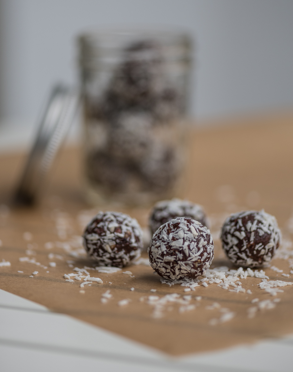 Vier schokoladige Bliss Balls mit Kokosflocken vor Glas