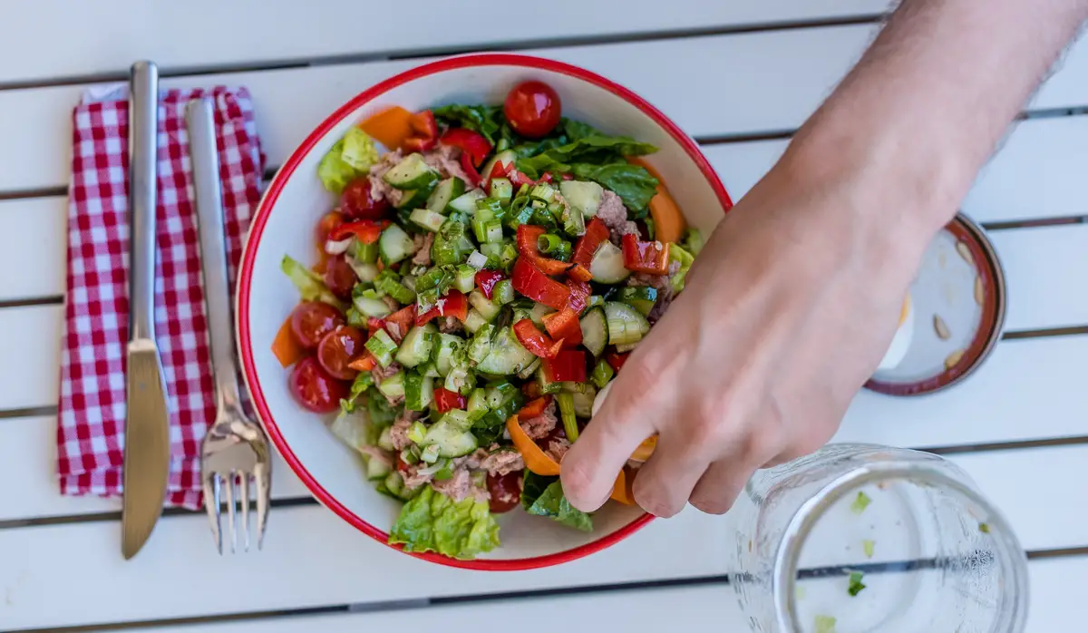 Top Shot von Salatteller und Hand, die Salat toppt