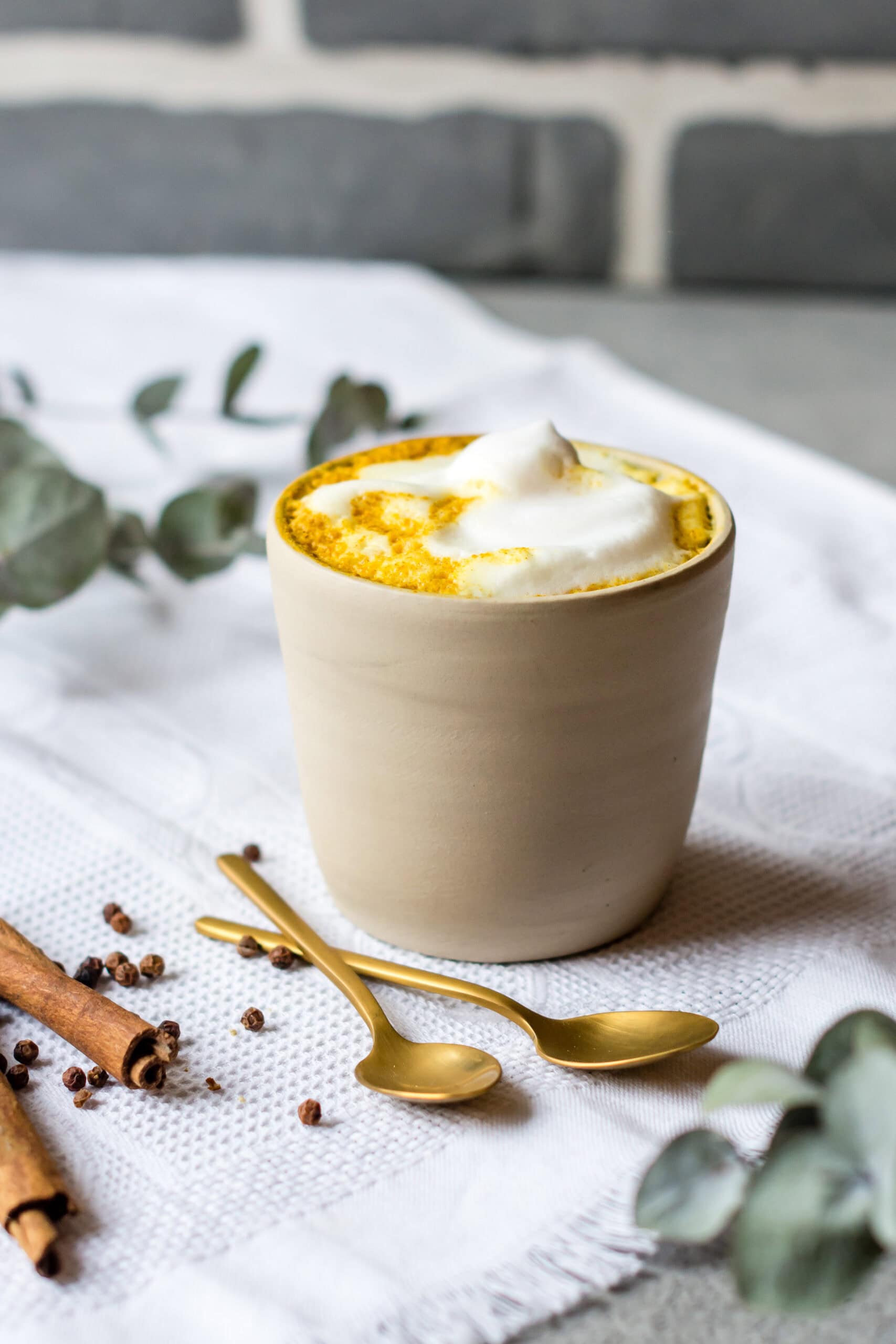 Keramikbecher mit Kurkuma Latte und Milchschaum.