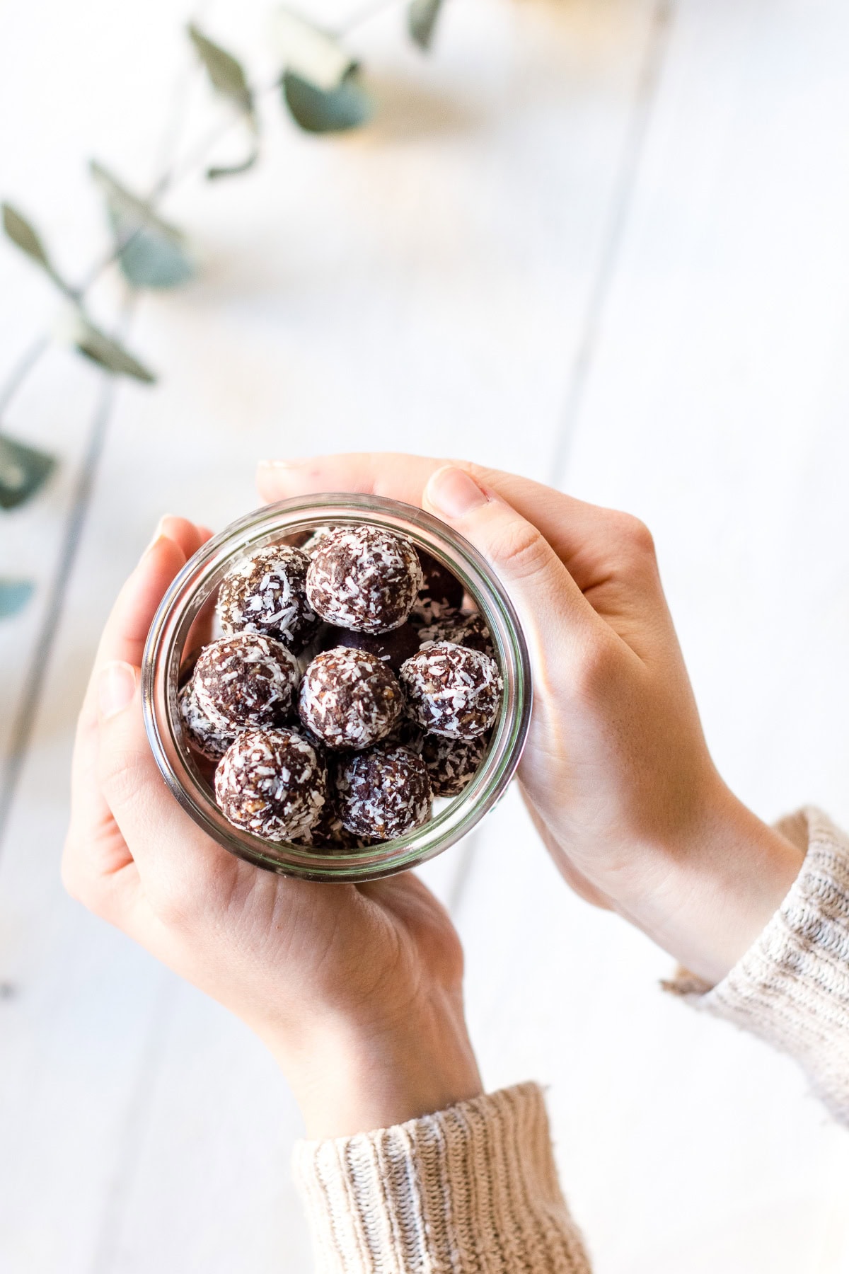 Hände halten ein Glas gefüllt mir Schokoladen Bliss Balls und Kokosstreuseln fest.