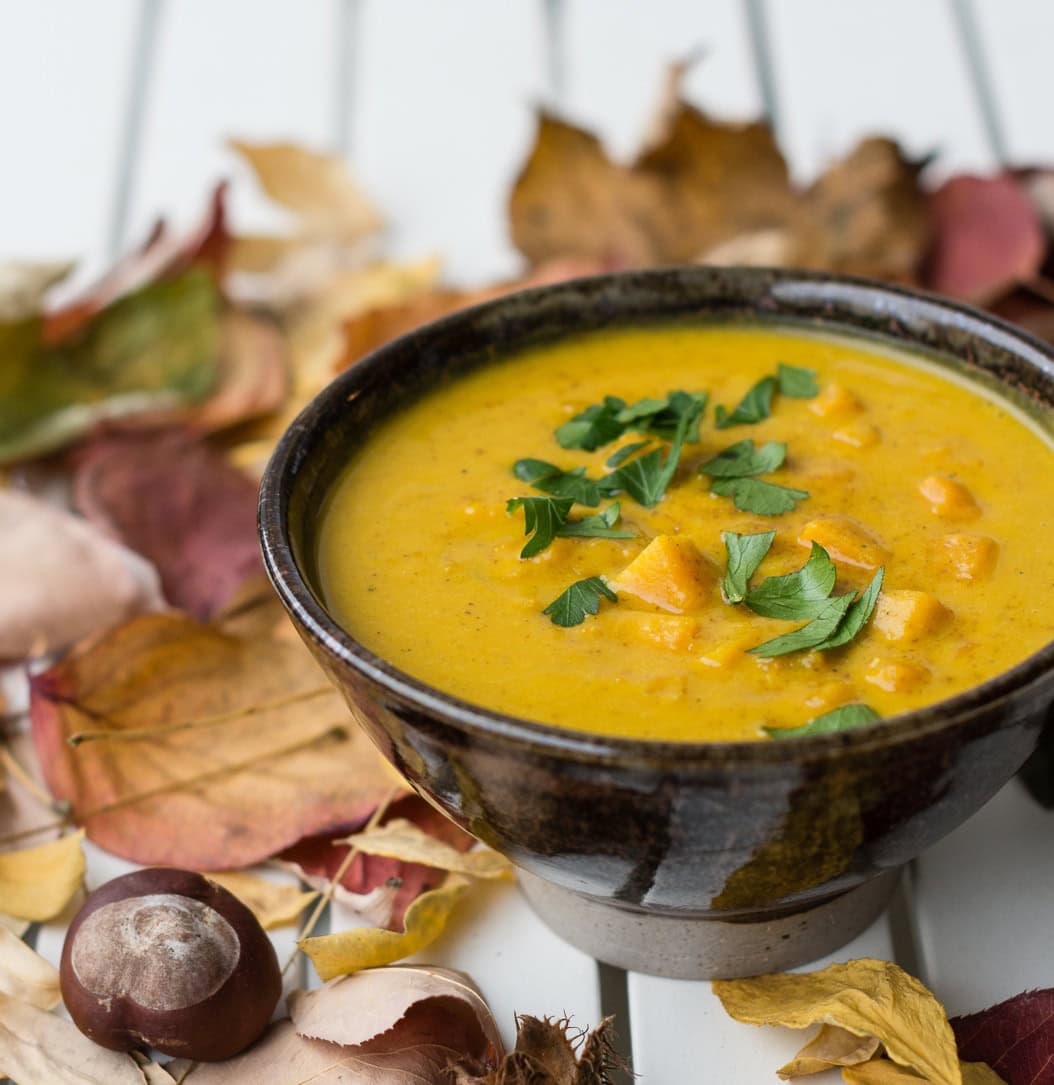 Gelbe Suppe in brauner Schale mit Petersilie garniert und auf Tisch mit Herbstblättern dekoriert