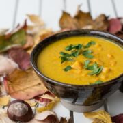 Gelbe Suppe in brauner Schale mit Petersilie garniert und auf Tisch mit Herbstblättern dekoriert