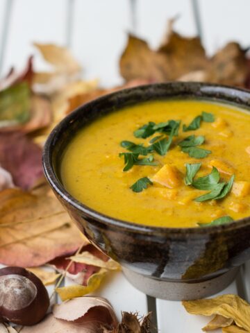 Gelbe Suppe in brauner Schale mit Petersilie garniert und auf Tisch mit Herbstblättern dekoriert