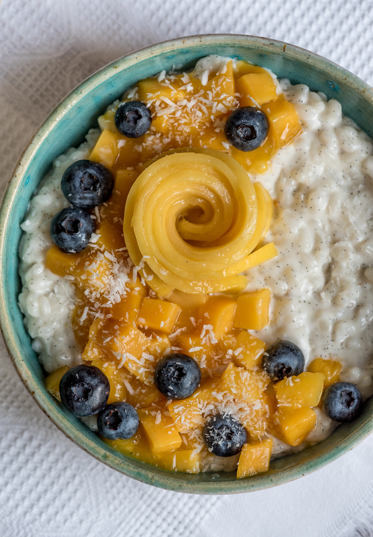 Topshot von Milchreis in Schüssel mit Mango und Blaubeeren getoppt