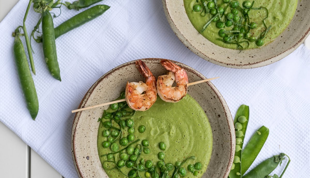 Topshot von zwei Suppentellern mit grüner Suppe, Erbsen und Garnelenspieß