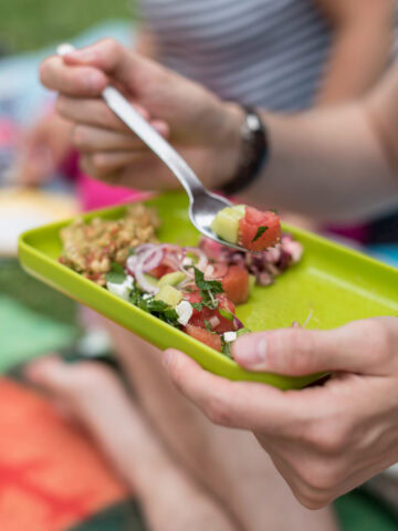 Hand hält knallgrünen Teller mit buntem Salat darauf