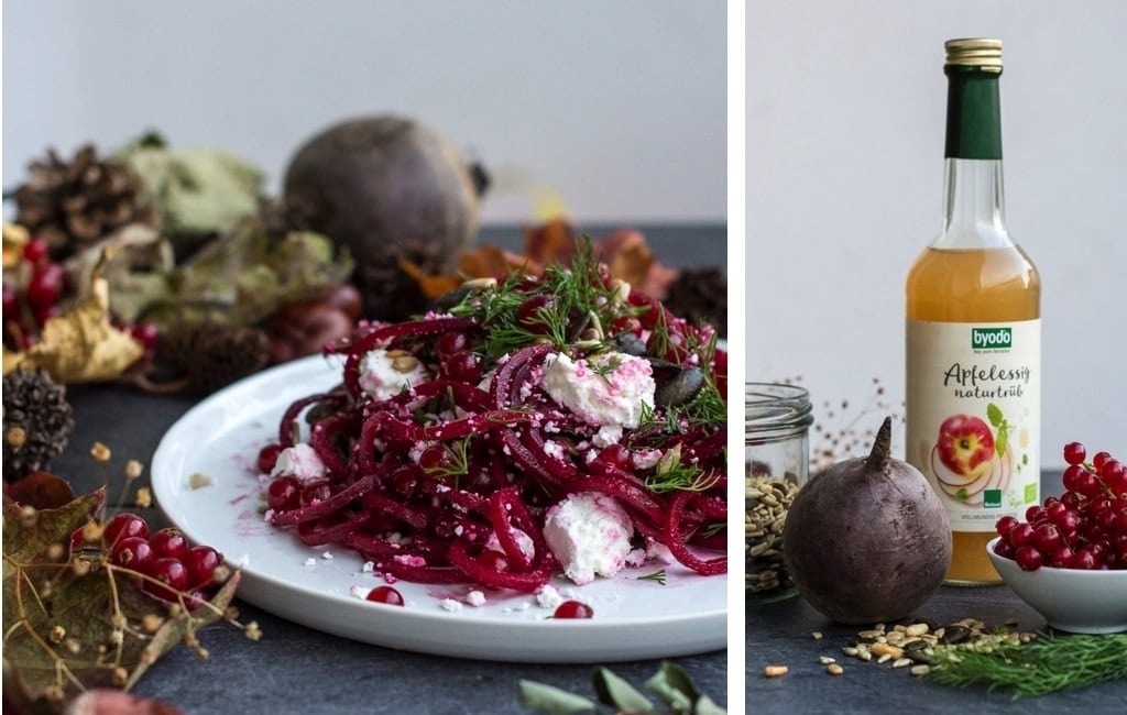 Closeup von Rote Bete Salat auf weißem Teller mit Ziegenkäse angerichtet und Foto von Apfelessig Flasche mit Roter Bete und Johannisbeeren dekoriert