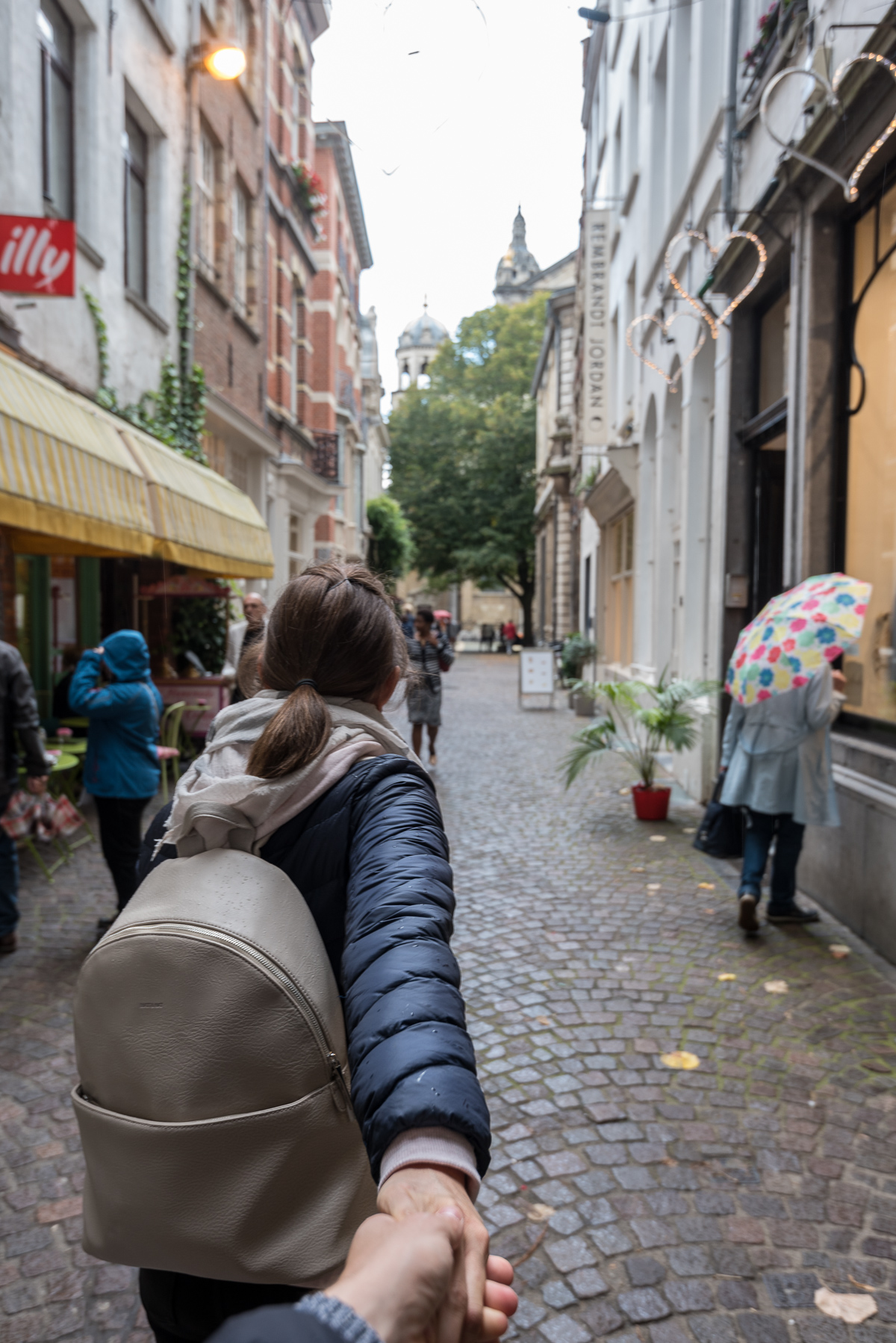 Frau zieht Person an Hand hinter sich durch die Straßen von Antwerpen