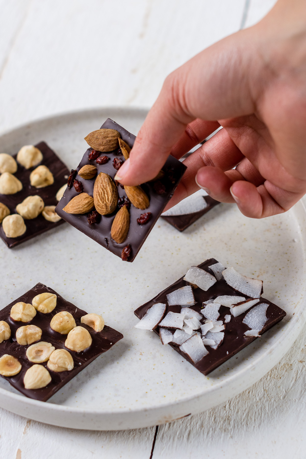 Hand hält ein Stück selbstgemachte Schokolade mit Nüssen und Beeren fest.