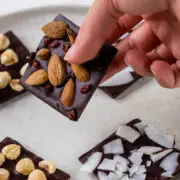 Hand hält ein Stück selbstgemachte Schokolade mit Nüssen und Beeren fest.