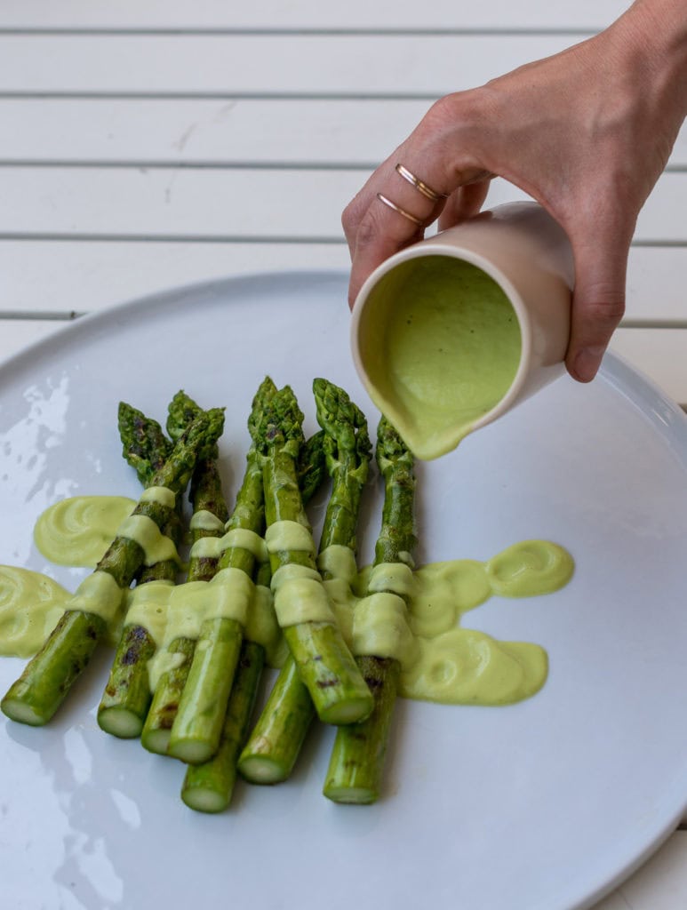 Hand übergießt grünen Spargel mit hellgrüner Sauce