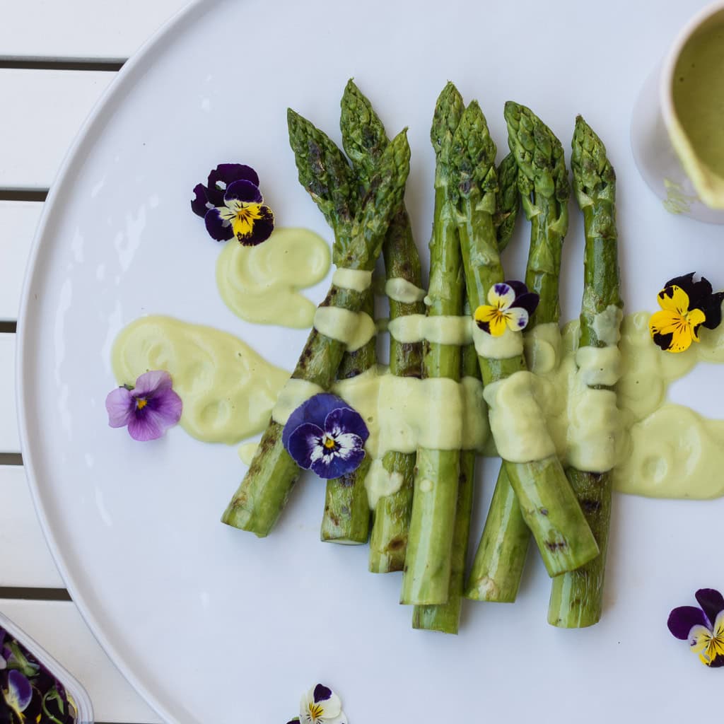 Grüner Spargel auf weißem Teller mit heller Sauce und Blumen