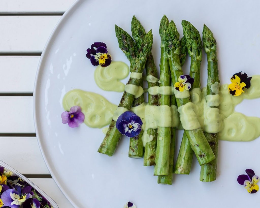 Grüner Spargel auf weißem Teller mit Sauce und Blumen angerichtet