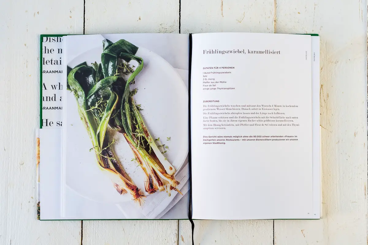 Aufgeschlagenes Kochbuch mit Foto und Rezept für karamellisierte Frühlingszwiebeln.