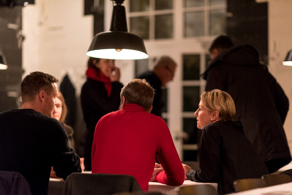 Personengruppe von hinten fotografiert, sitzt an einem Tisch und unterhält sich.