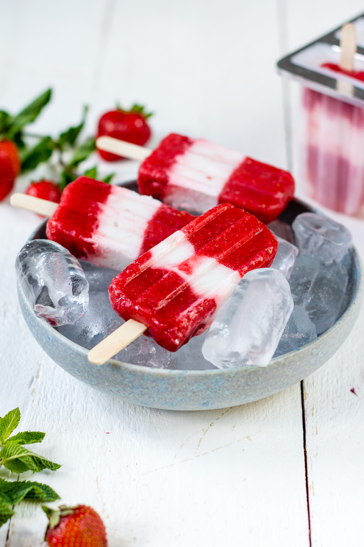 selbstgemachte Erdbeer Joghurt Popsicles in einer Schale mit Eiswürfeln.