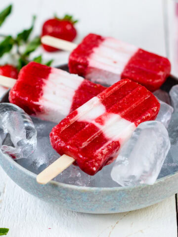 selbstgemachte Erdbeer Joghurt Popsicles in einer Schale mit Eiswürfeln.