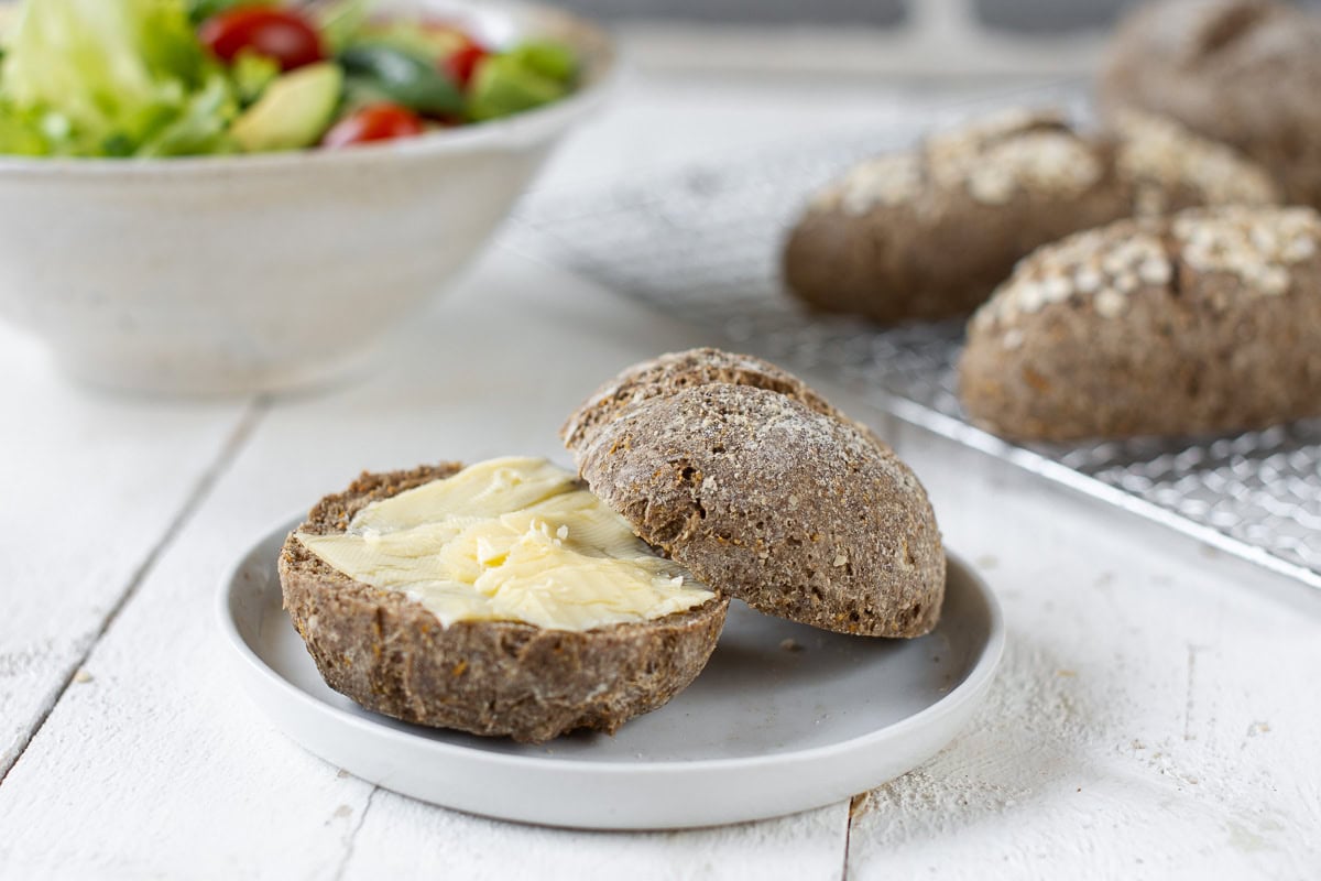 Ein weißer Teller mit einem aufgeschnittenem Brötchen mit Butter bestrichen.