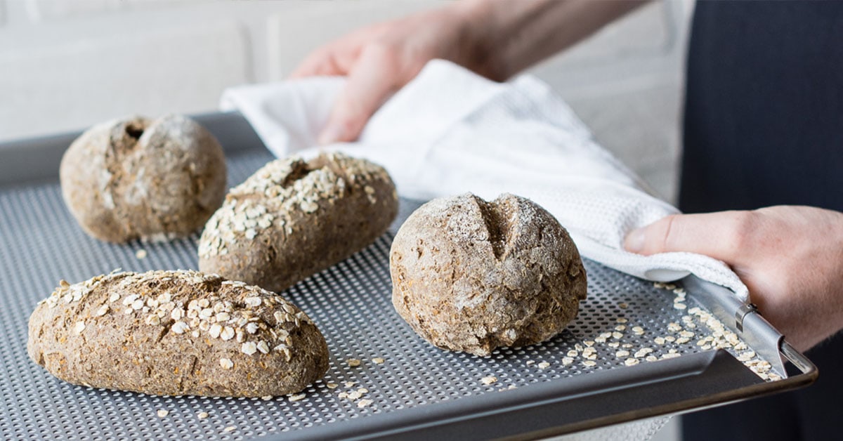 Gehaltenes graues Backblech mit vier dunklen Brötchen