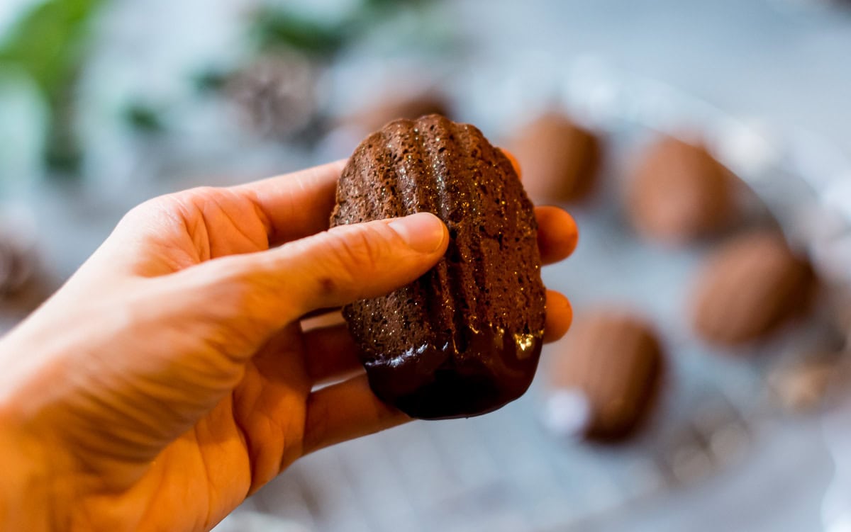 Hand hält ein Schokoladen Madeleines mit Schokoladenüberzug fest.