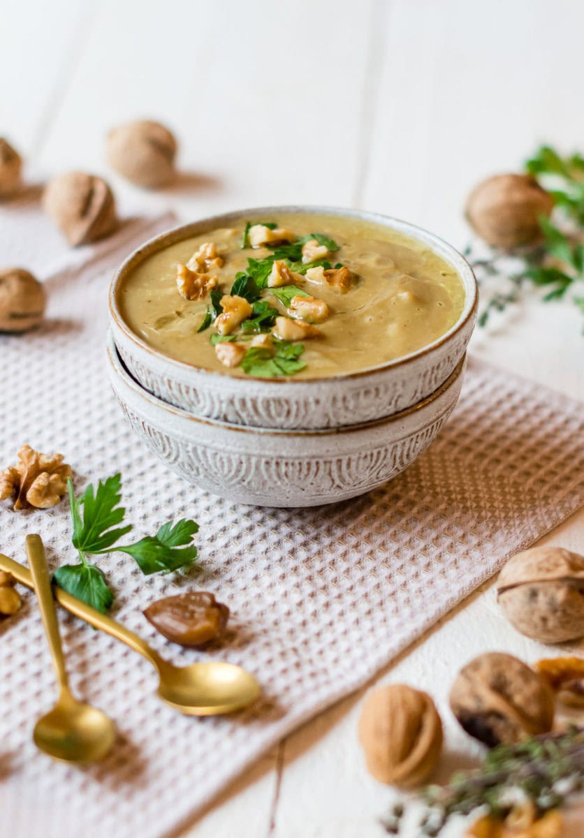 Zwei Schüsseln mit Maronensuppe und Walnüssen und frischen Kräutern.