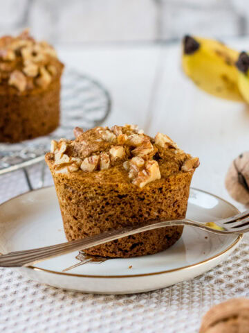 Glutenfreie Bananenmuffins mit Walnüssen und Zimt auf kleinem Teller mit Bananen und Muffins im Hintergrund.