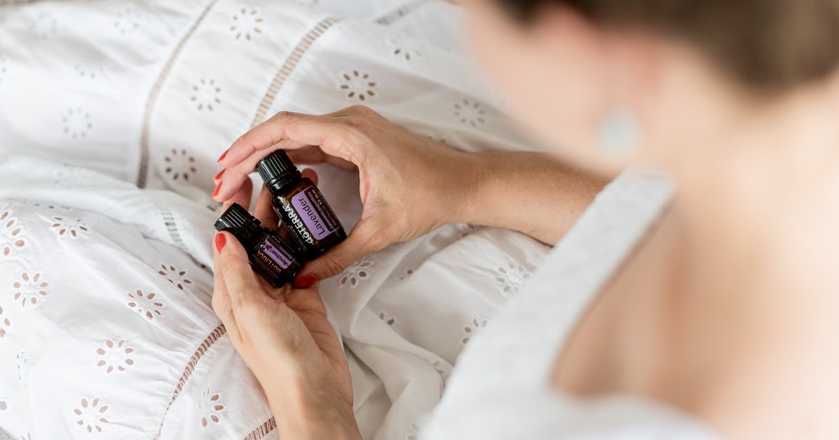 Frau im weißen Kleid mit zwei ätherischen Ölen von dōTERRA in der Hand.