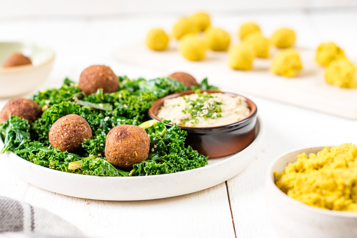 Pinne das Foto, um das Rezept schnelle Falafel mit Hummus und Grünkohl zu speichern! Schnelle Curry-Falafeln mit gebratenem Grünkohl und Hummus, im Hintergrund Falafel Bällchen vor dem Backen