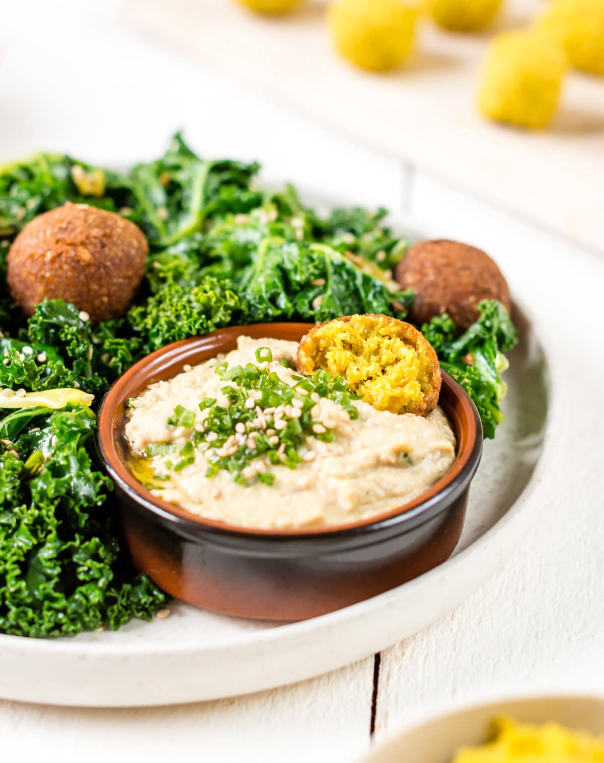 Pinne das Foto, um das Rezept schnelle Falafel mit Hummus und Grünkohl zu speichern! Schnelle Curry-Falafeln mit gebratenem Grünkohl und Hummus, im Hintergrund Falafel Bällchen vor dem Backen