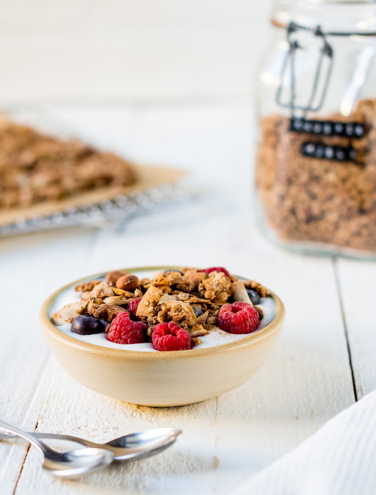 Selbstgemachtes Granola in einer Müslischale mit Joghurt, Beeren und Knuspermüsli auf weißem Untergrund.