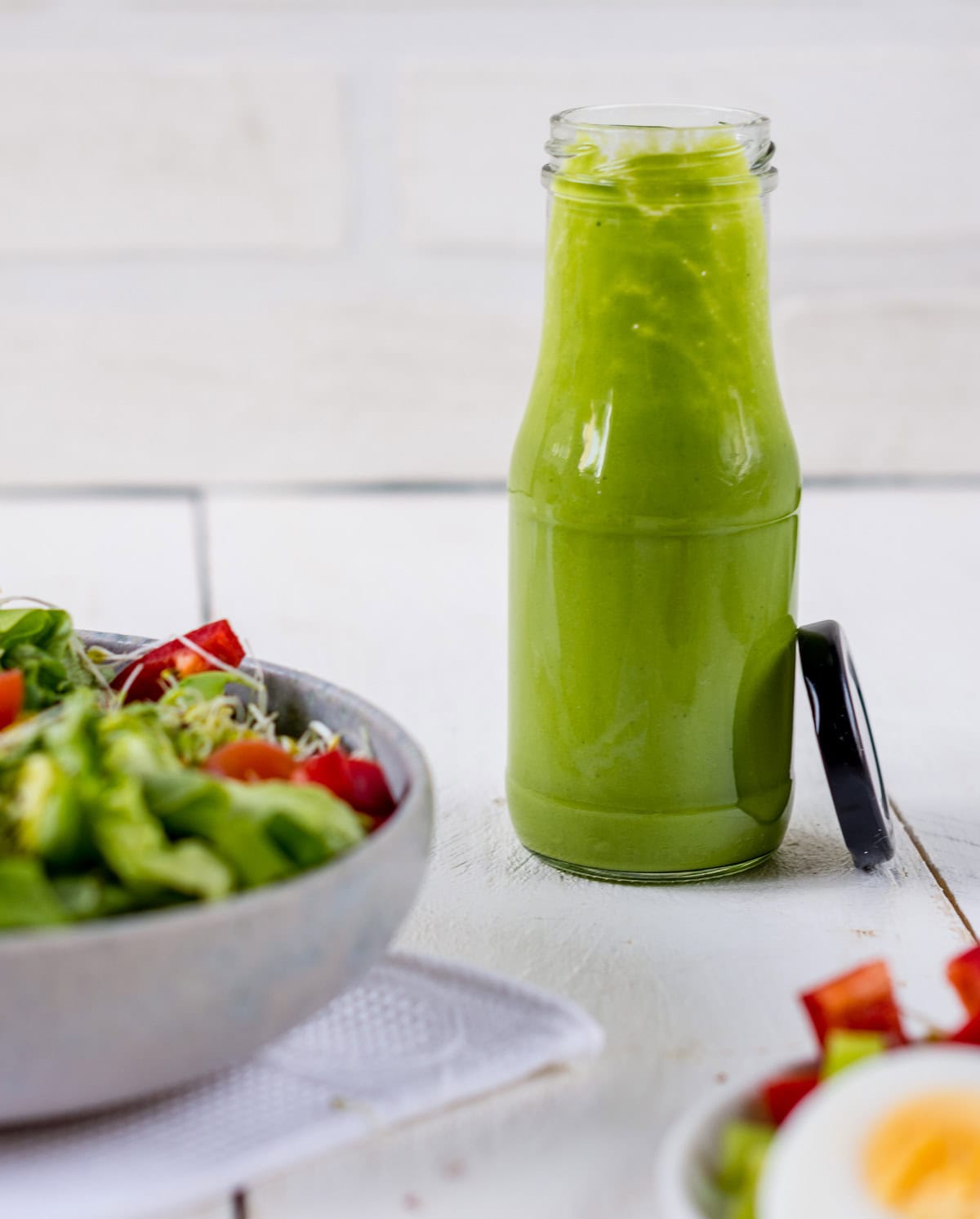 Pinne das Foto, um das Rezept für das Avocado Kräuter Dressing zu speichern! Offene Flasche mit grünem Salatdressing.