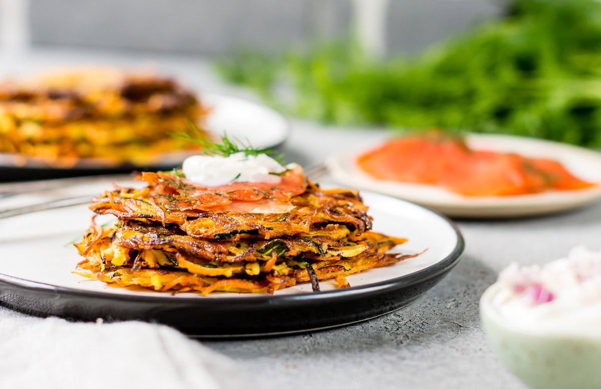 Speichere dieses Foto, um das Rezept für knusprige Zucchini Möhren Puffer zu sichern! Teller gefüllt mit Zucchini Möhren Puffern und frischem Lachs und Kräuterquark.