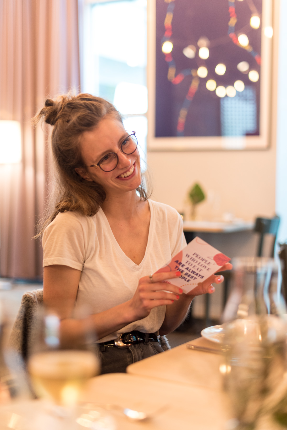 Frau sitzt an einem Tisch und lächelt und hält eine Postkarte in der Hand.