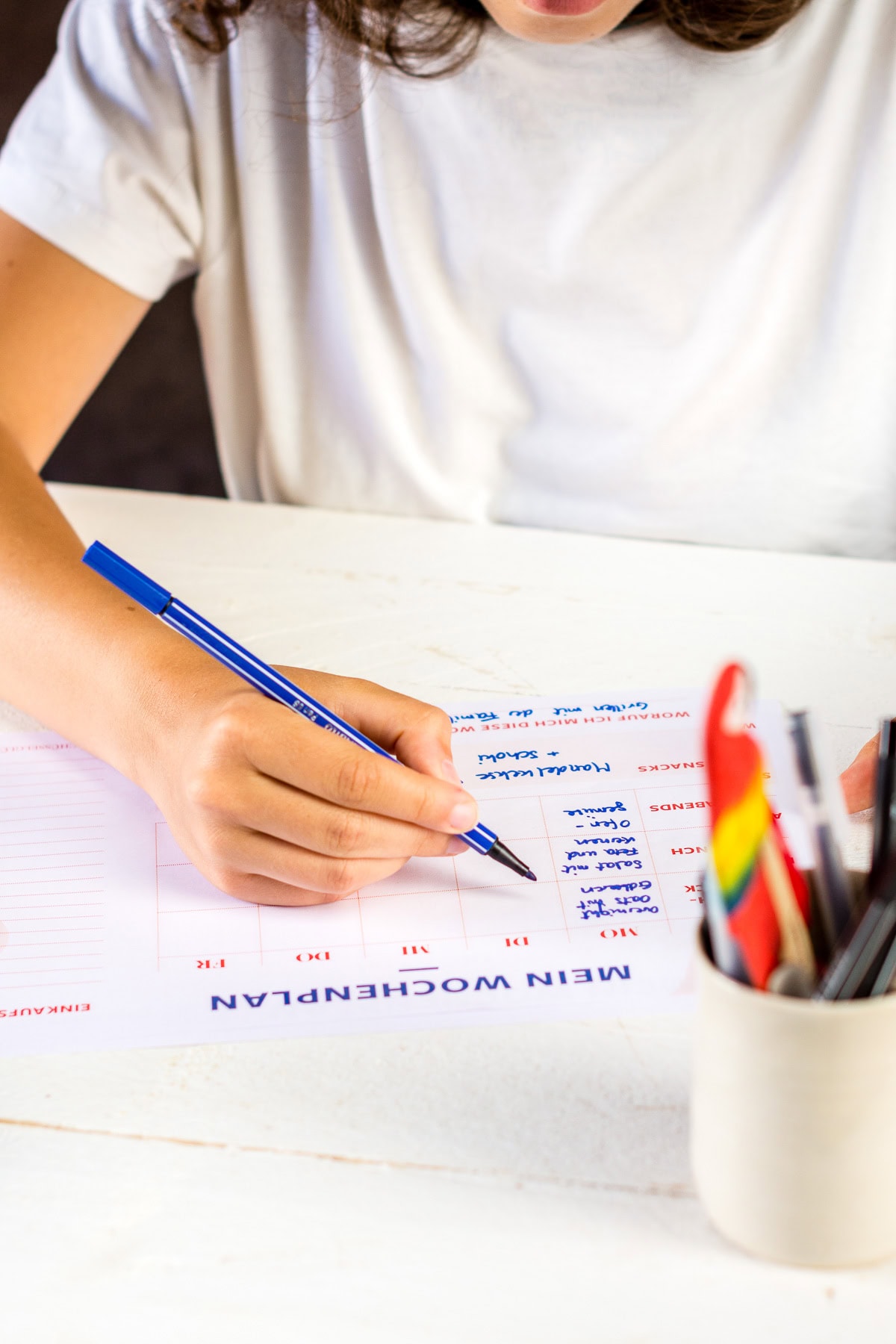 Hand, die einen Stift hält und einen Wochenplan ausfüllt.