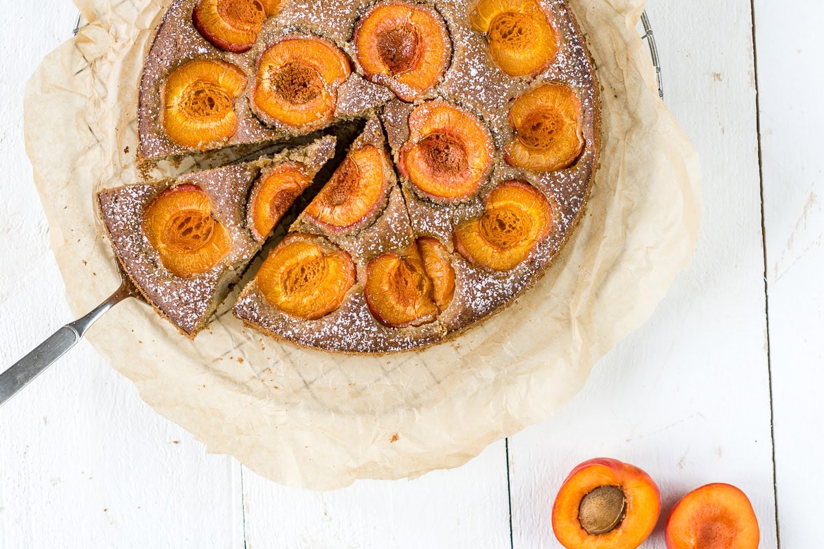 Bild von oben von einem Aprikosenkuchen mit einer Kuchengabel auf weißem Untergrund. und Backpapier