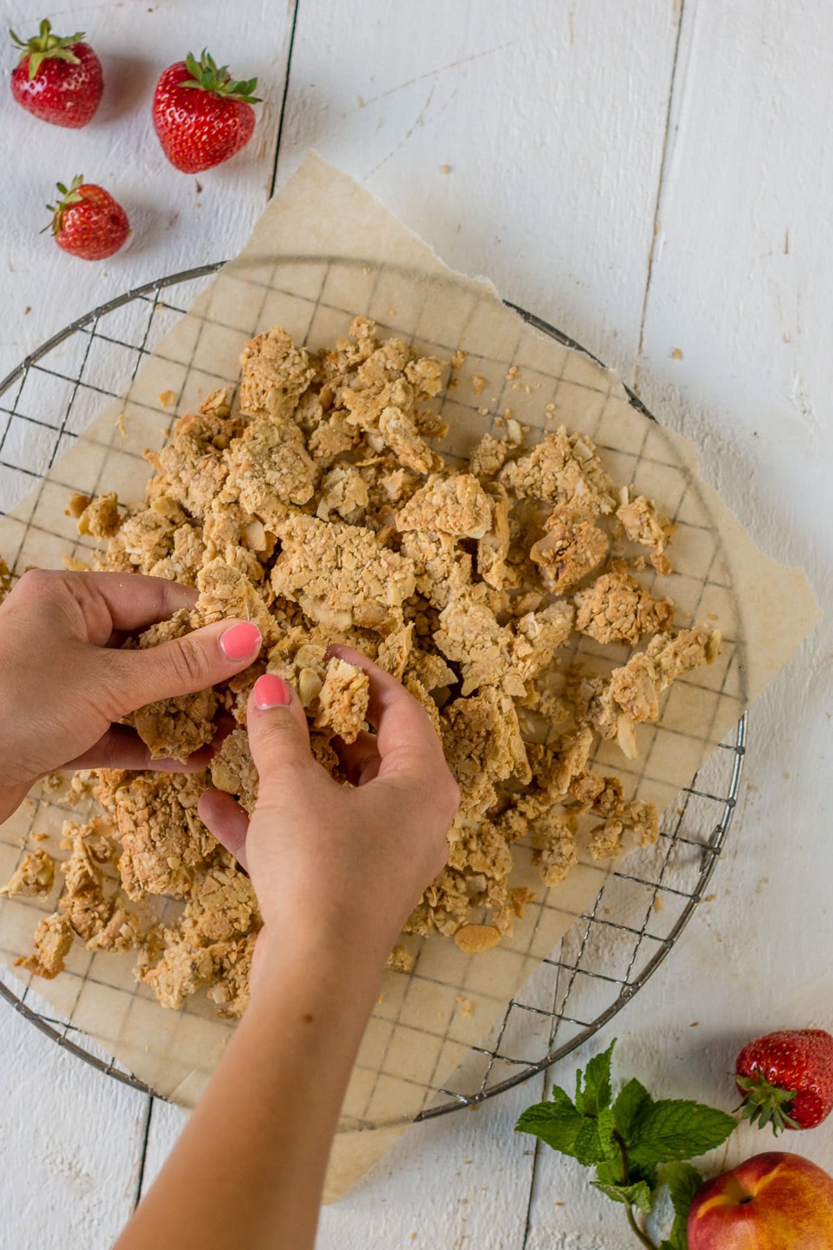 Pinne das Foto, um das Rezept für glutenfreies Granola zu speichern! Bild von oben von einem Rostgitter mit Müsliteig der mit den Händen zerbrochen wird.